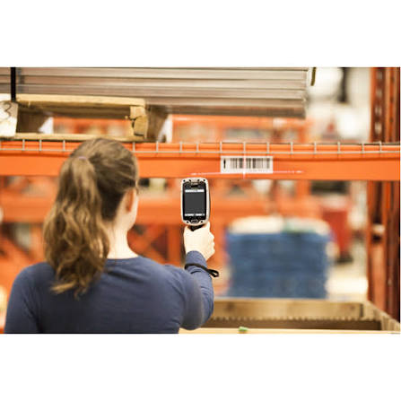 A warehouse worker aiming a Zebra TC8000 at a barcode label on an orange
                  racking beam from a couple of metres away, the aiming line visible across
                  the label